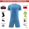 A promotional product graphic for a Chief Soccer Kit premium deal, showing a light blue soccer jersey and matching shorts centered on a white background, surrounded by included accessories: a black and red kit bag, black soccer socks, a black whistle, a white training ball, a red captain armband, a neon green GK kit, and a pair of white and green gloves. Text labels identify each item, with a red header reading 'CHIEF SOCCER KIT | PREMIUM DEAL' and a Grip Sport logo at the bottom right.